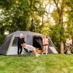 A group of people standing around a 12 person instant cabin tent with full rainfly  in a forested area.