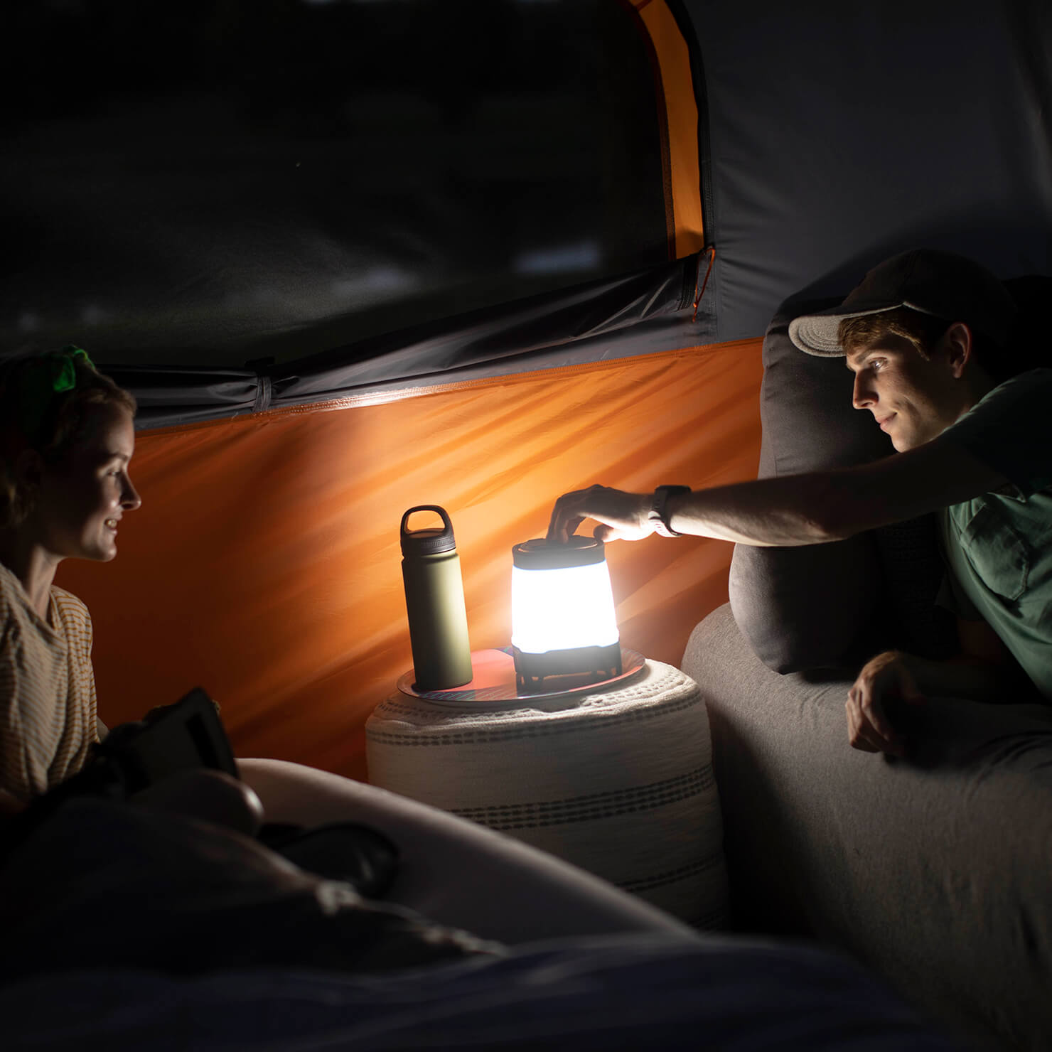 Campers using CORE 1250 lumen rechargeable lantern with Bluetooth speaker for light and music in tent.