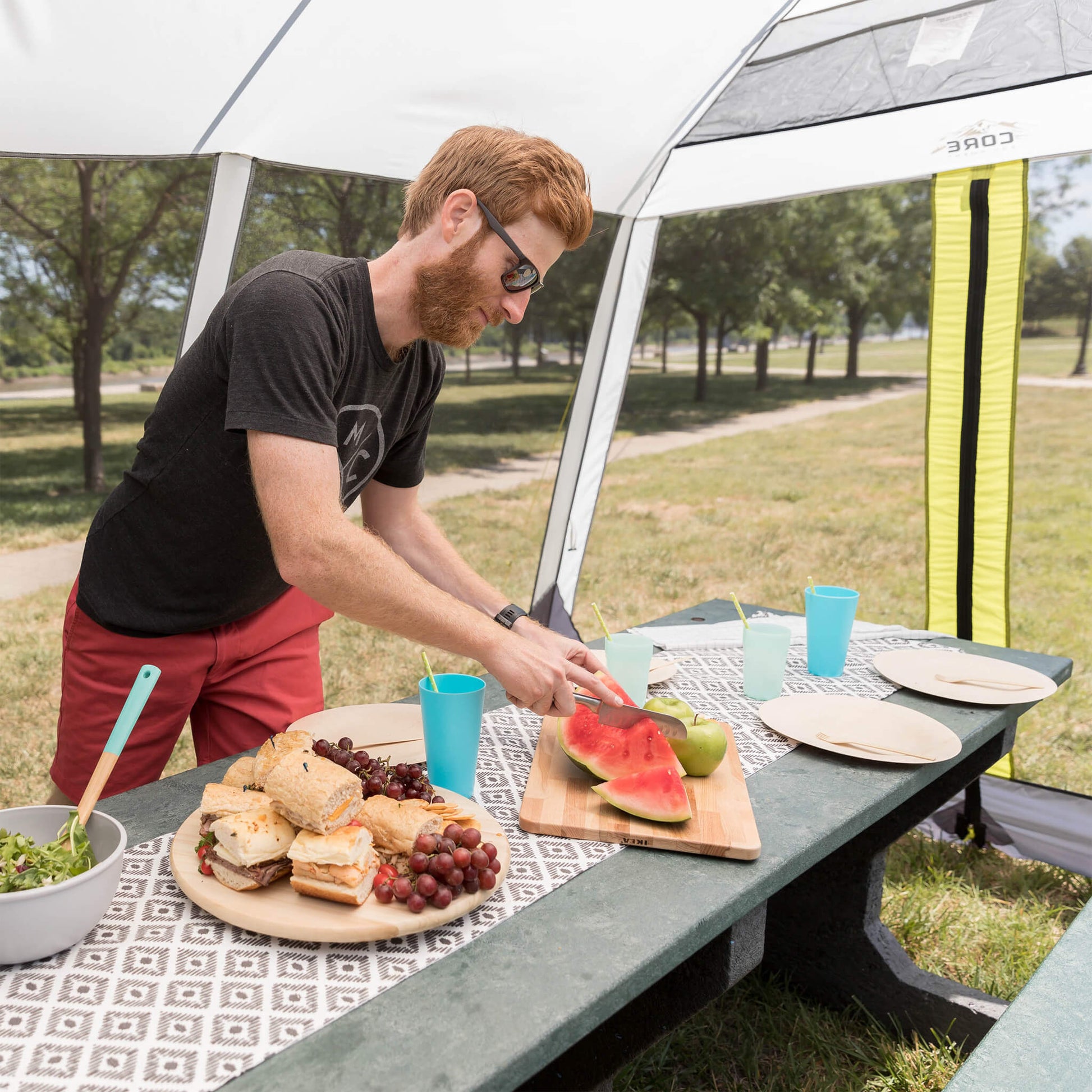 Camper preparing food inside CORE 12x10 instant screen house with mesh walls, enjoying shade and bug-free protection outdoors.
