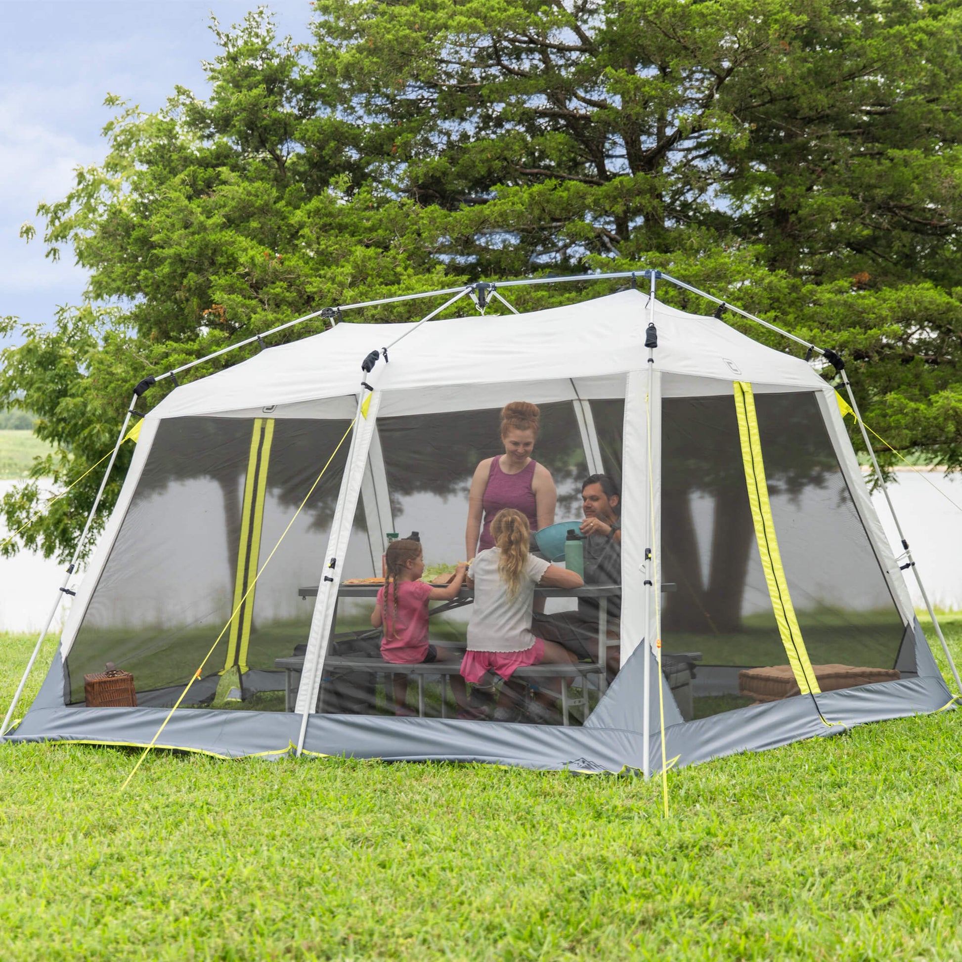 Family enjoying shade inside CORE 12x10 instant screen house with mesh walls, perfect for picnics, camping, or backyard gatherings.