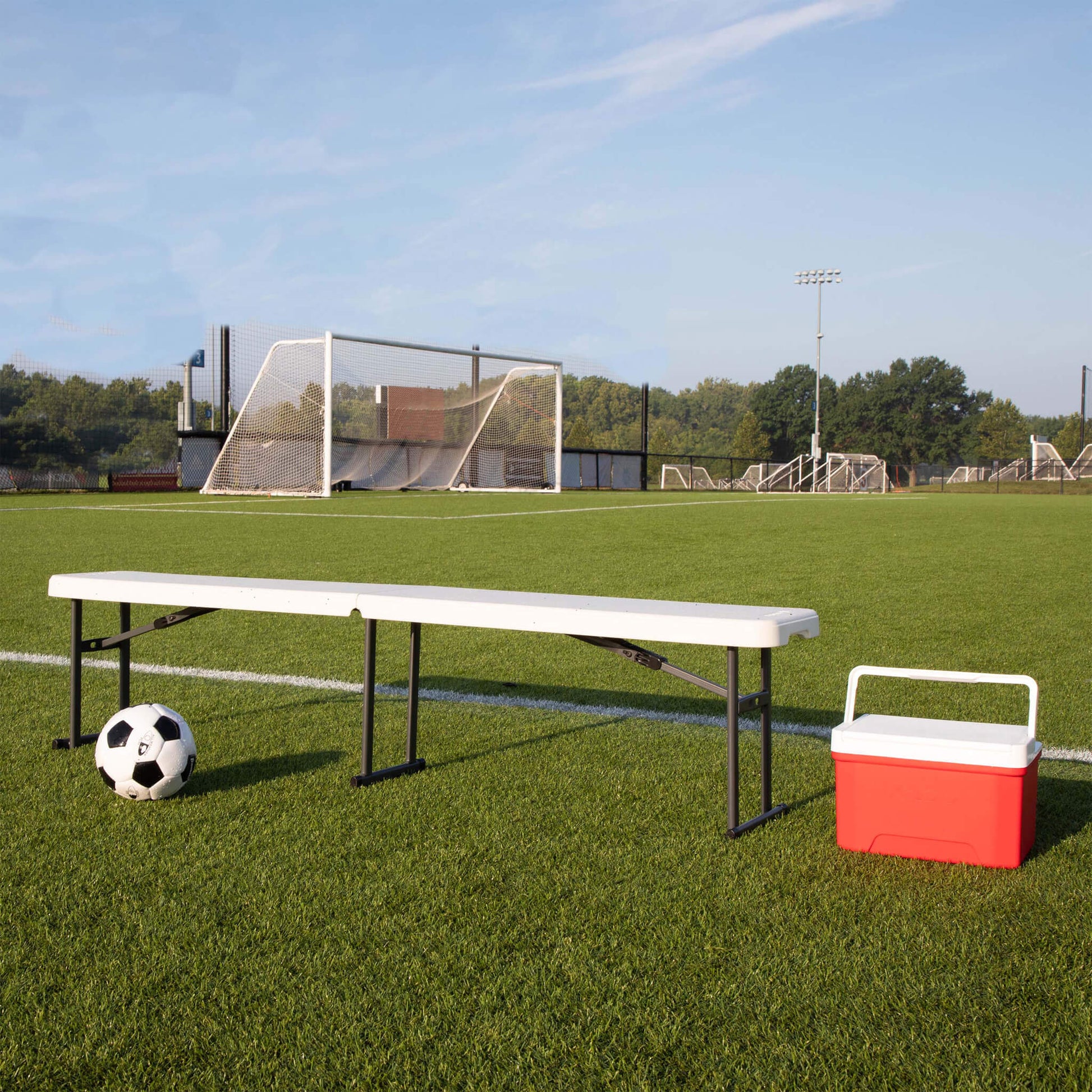 CORE folding bench on soccer field with ball and cooler beside it, providing portable seating for games, camping, or events.
