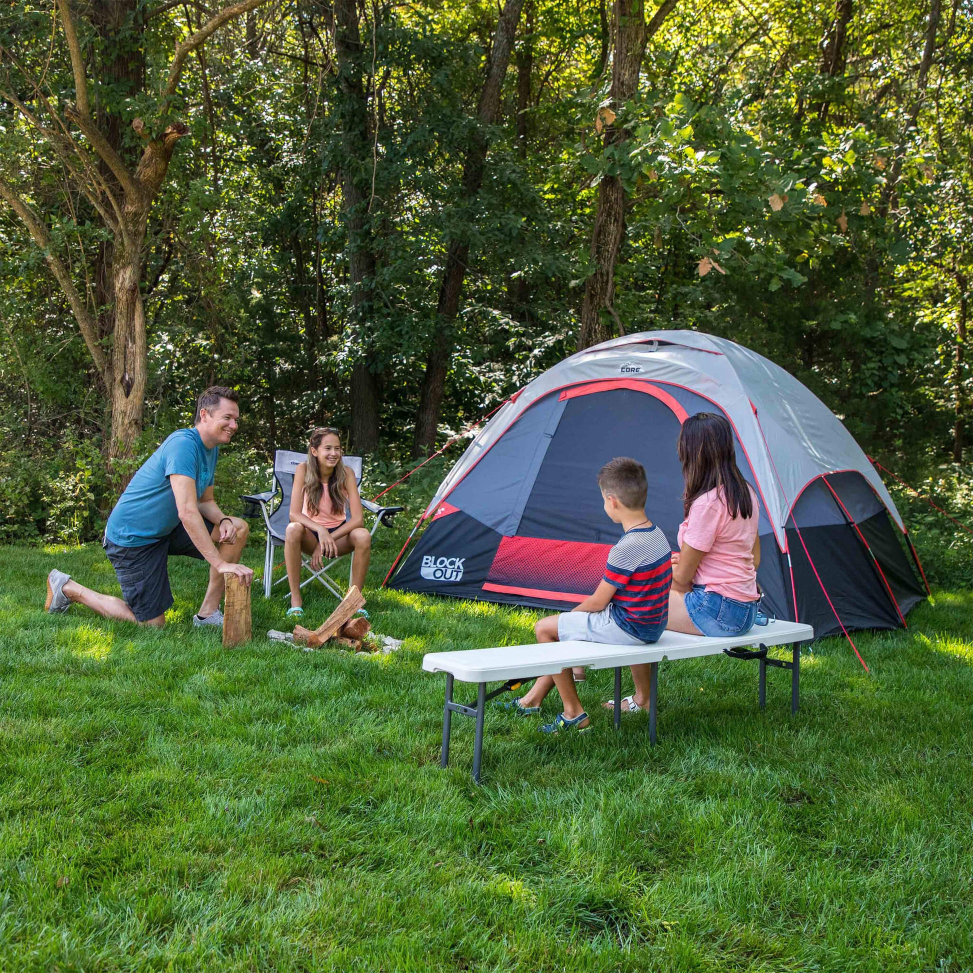 Family sitting outdoors beside CORE folding bench, shown at campsite near a tent for portable seating during activities.