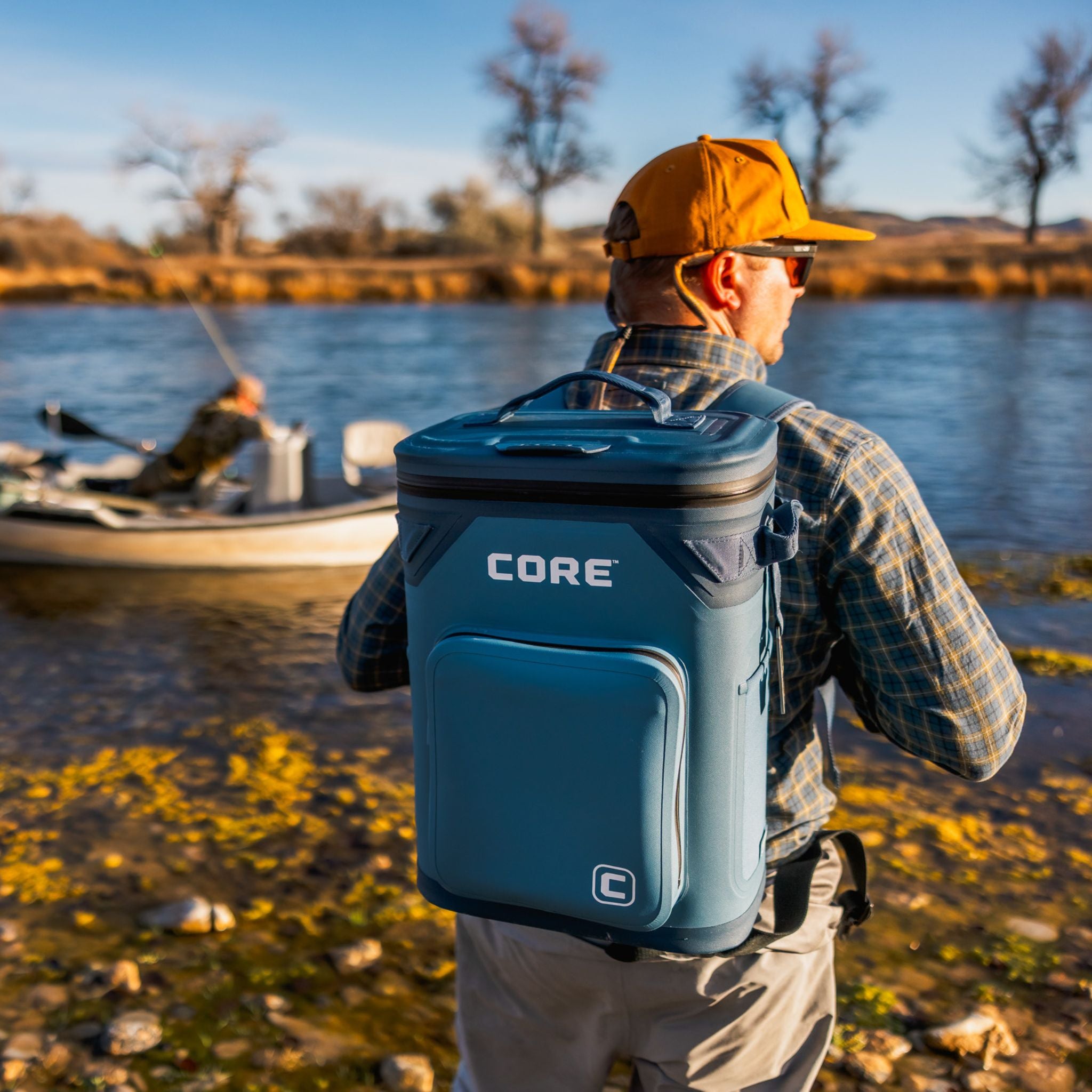 A man with a blue Climakeep cooler backpack labeled 'CORE' by a lake.