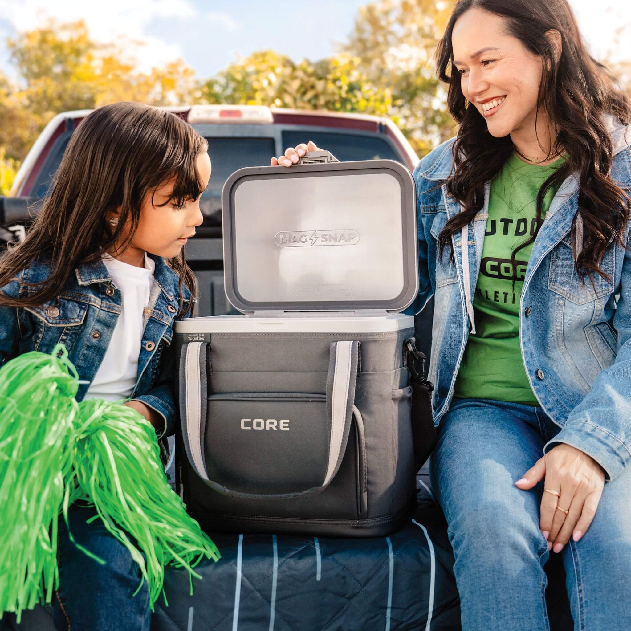 Lifestyle image of an adult and child at a truck tailgate with an open CORE soft cooler, showing easy access in a family-friendly outdoor setting.