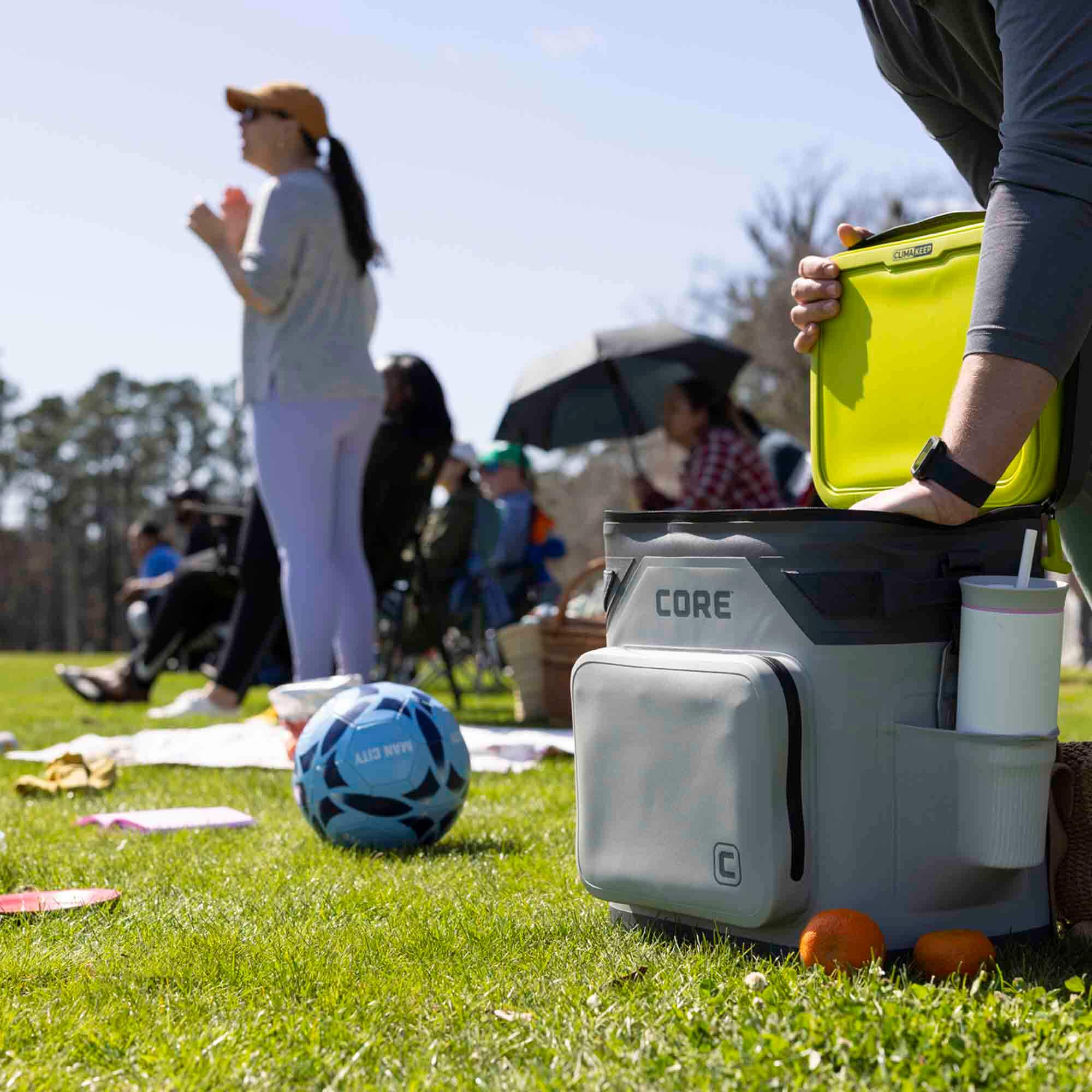 Person using CORE Climakeep 36 can shadow gray cooler at a soccer game and cooler open with bright green lid.