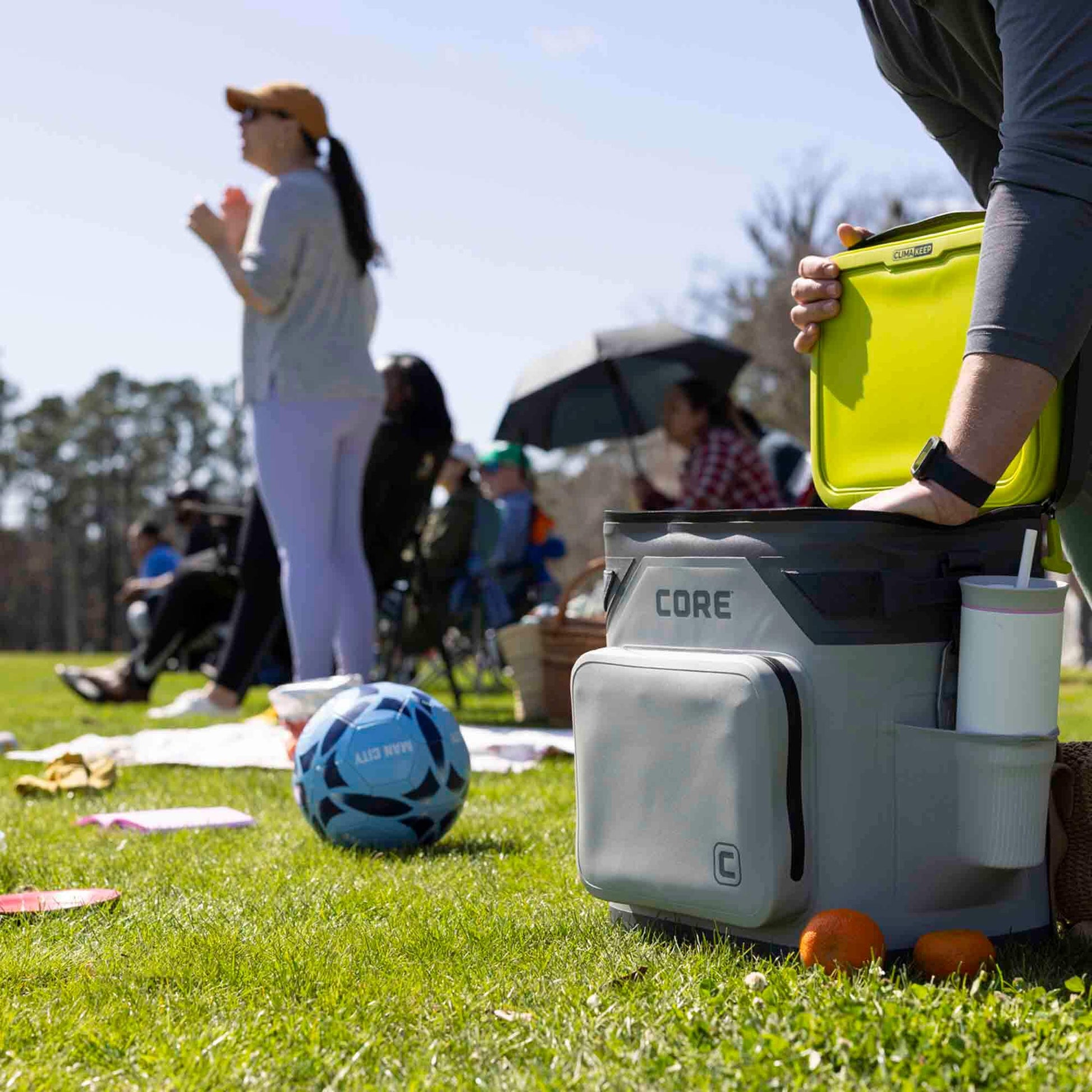 Person using CORE Climakeep 36 can shadow gray cooler at a soccer game and cooler open with bright green lid.