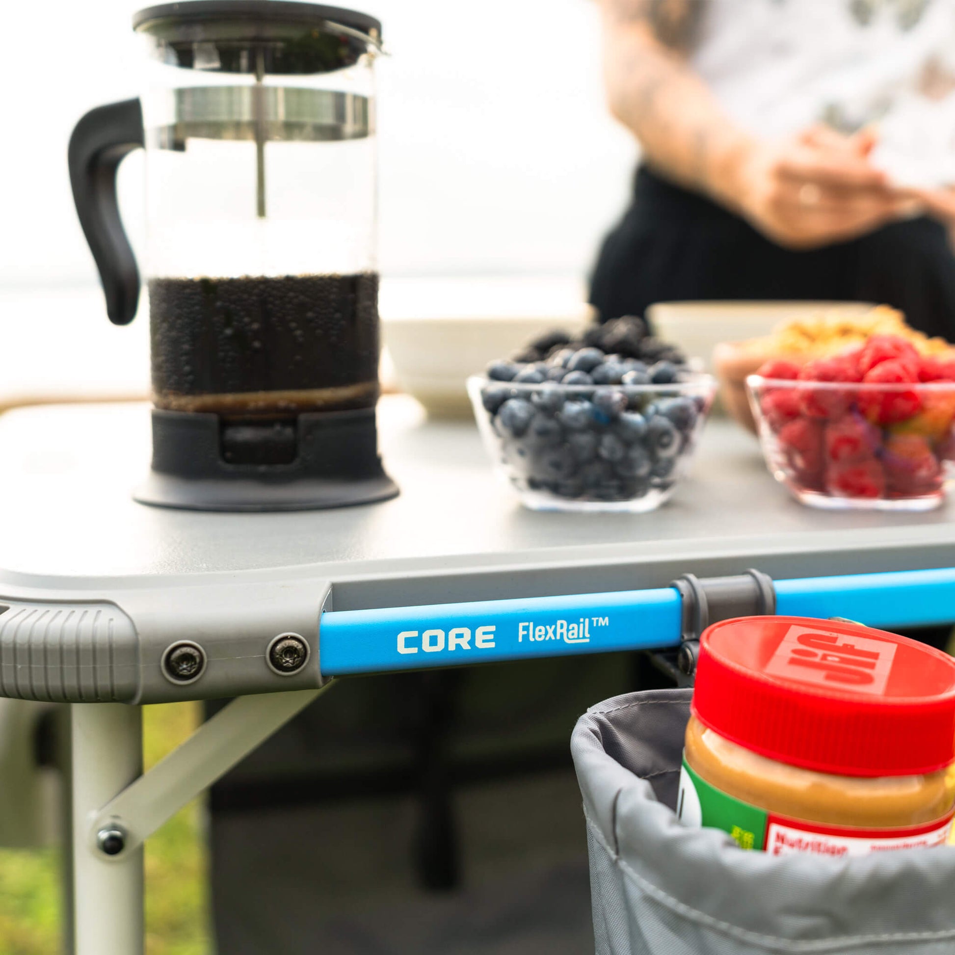 Close-up of CORE camp table with FlexRail system, uitlity basket, and food items placed on top.