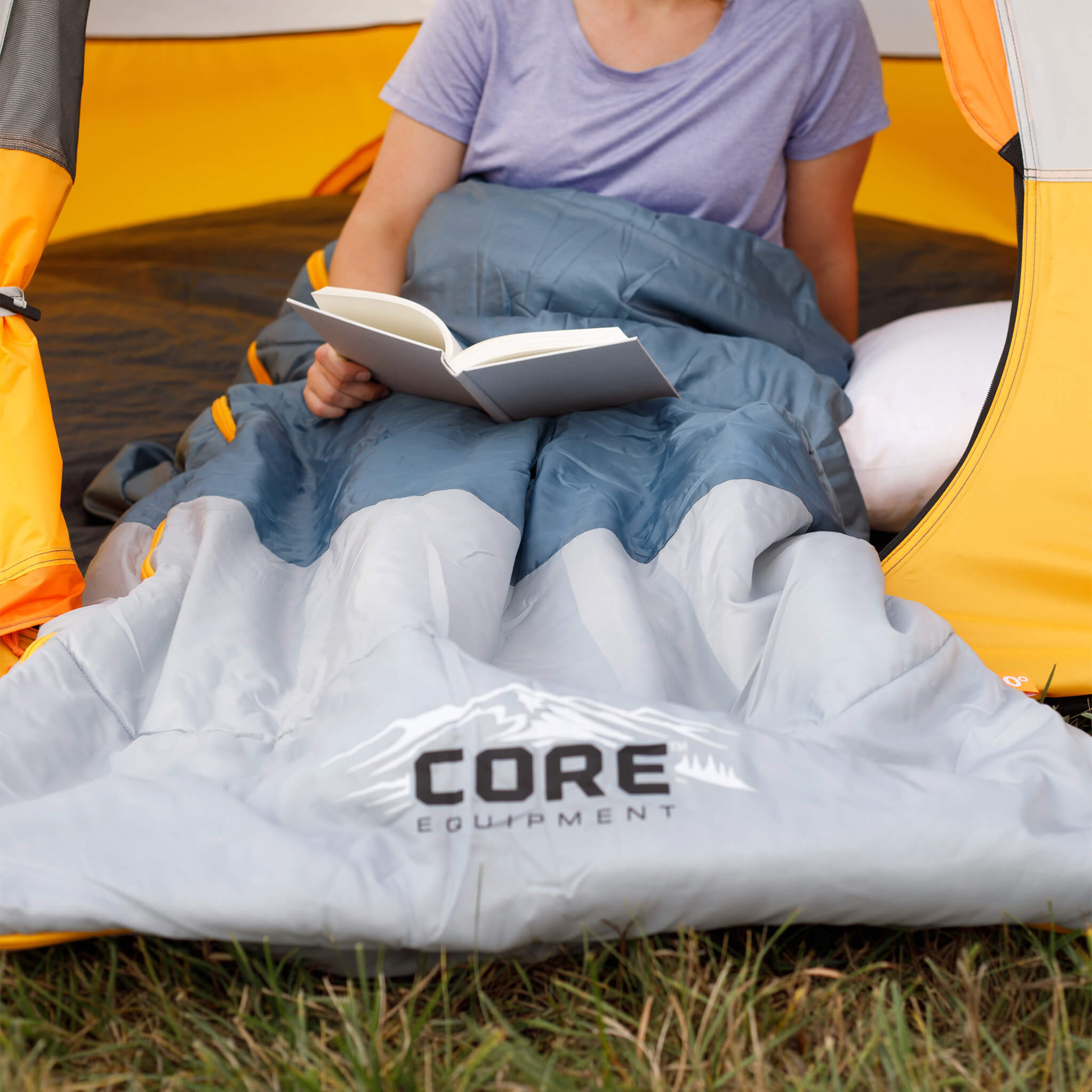 A camper reading inside CORE 3 person dome tent tent while lying in CORE 50 Degree sleeping bag.
