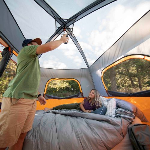 Two people inside a camping tent with a clear view of trees outside.