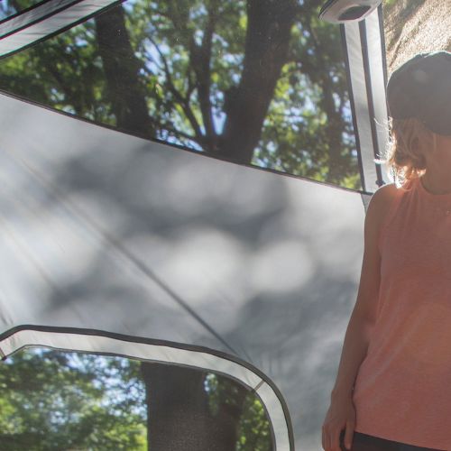 A person is standing inside a tent with a rainfly off looking through the mesh ceiling into the sky.
