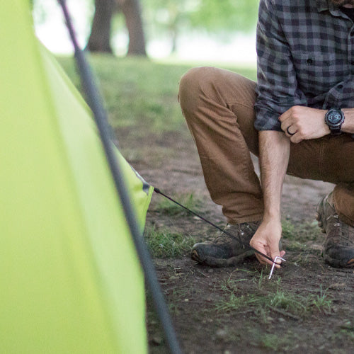 Close-up of a CORE 6 person instant tent ventilation showing durable green fabric, reinforced seams, and a person guying out with a stake.