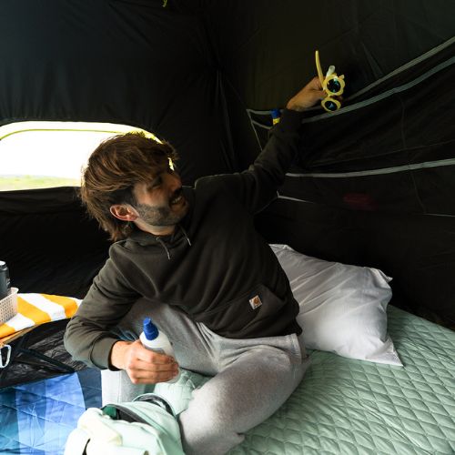 A person sitting inside a CORE 6 person blockout instant tent putting glasses in wall organizer.