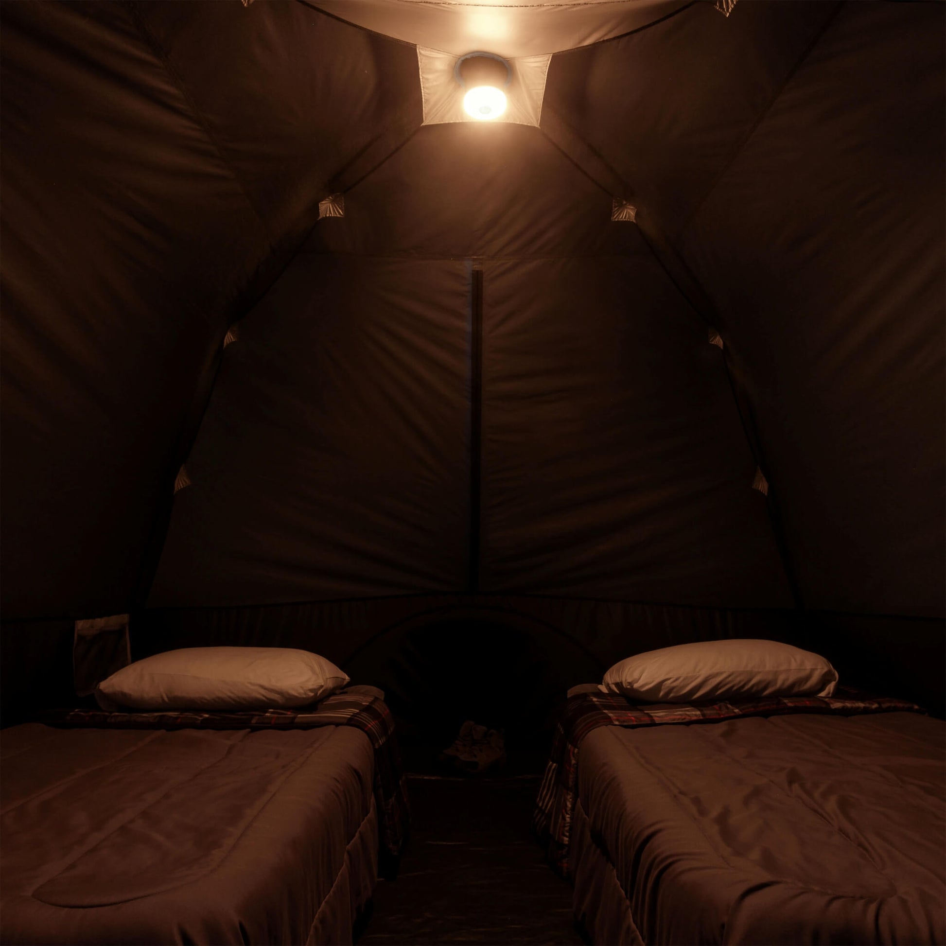 Inside view of CORE 6 person lighted dome tent with two cots, dark interior, and ceiling light on amber mode providing overhead illumination.