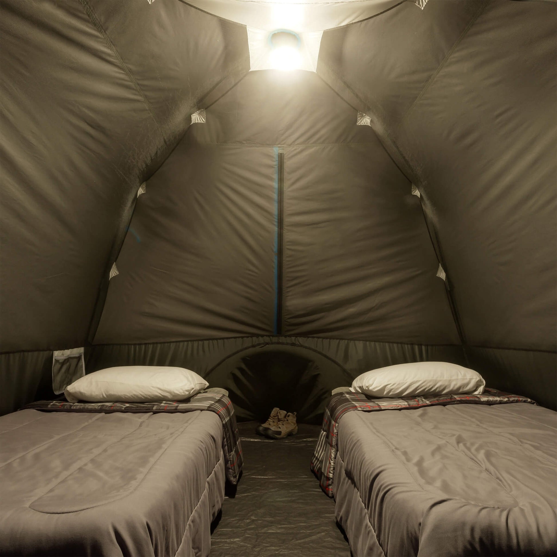 Inside view of CORE 6 person lighted dome tent with two cots, dark interior, and ceiling light on high mode providing overhead illumination.