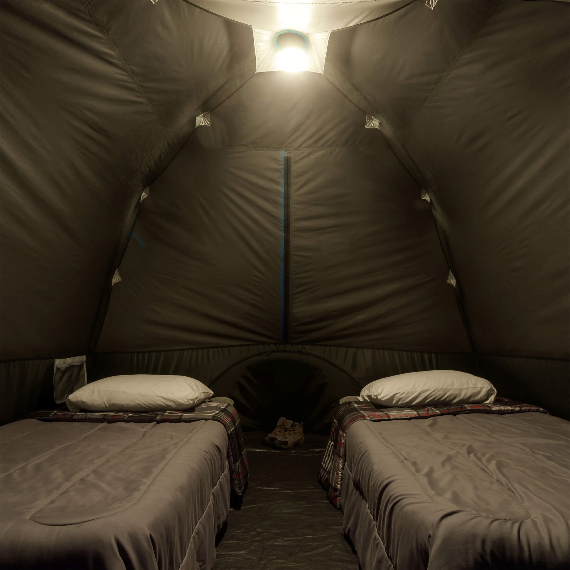 Inside view of CORE 6 person lighted dome tent with two cots, dark interior, and ceiling light on low mode providing overhead illumination.