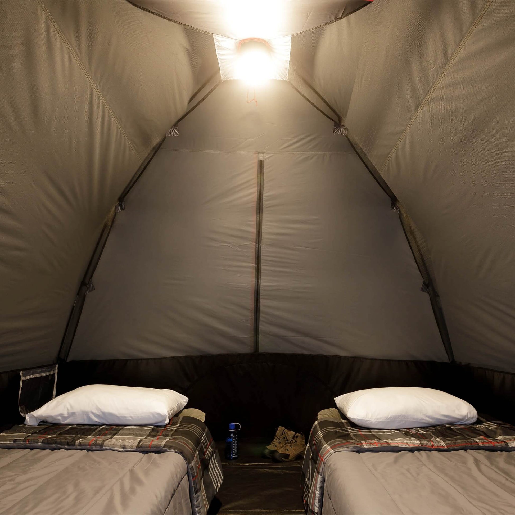 Inside view of CORE 6 person lighted dome tent with two cots, dark interior, and ceiling light on high mode providing overhead illumination.