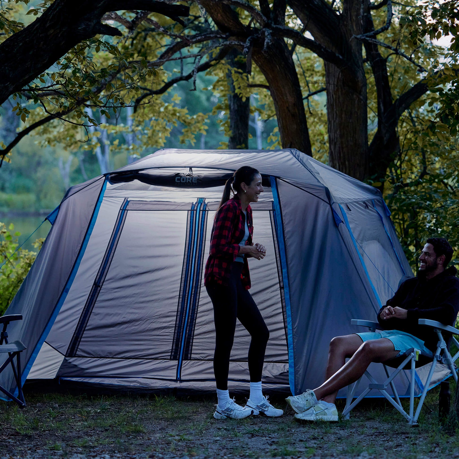 Campers relaxing beside the CORE 6 person lighted instant cabin tent with full rainfly in blue and gray, designed for fast setup and reliable weather protection.