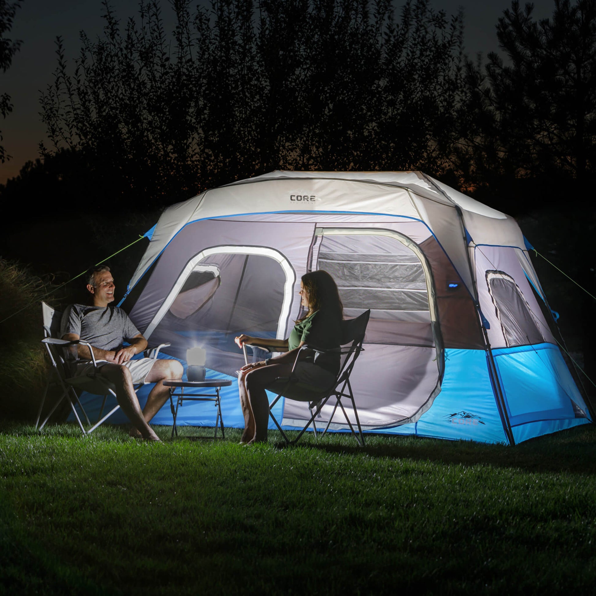 Campers relaxing beside the CORE 6 person lighted instant cabin tent in blue and gray, designed for fast setup and reliable weather protection.