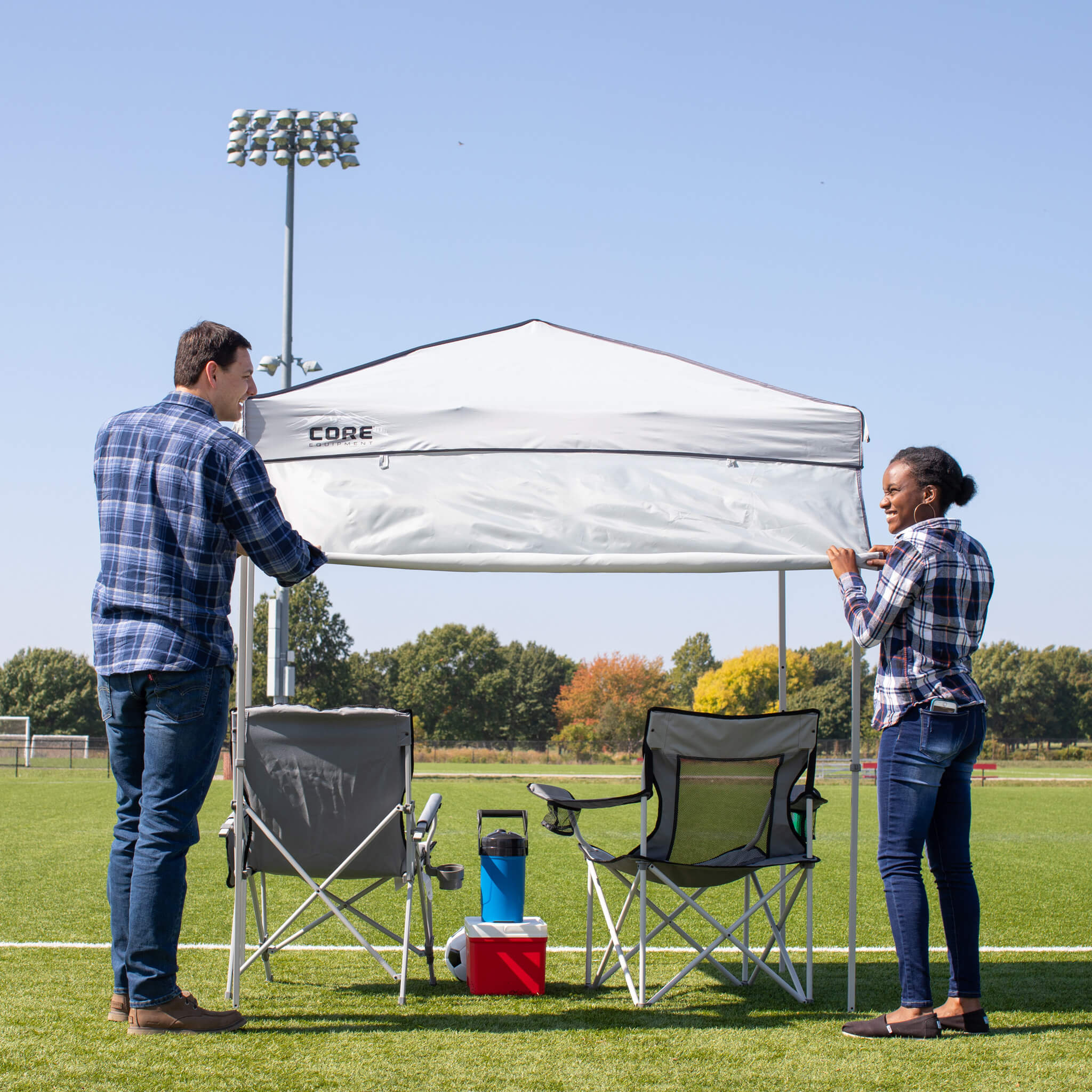 Campers setting up CORE 6x4 instant canopy in gray with steel frame and rollable sun wall, perfect for shade at games or picnics.