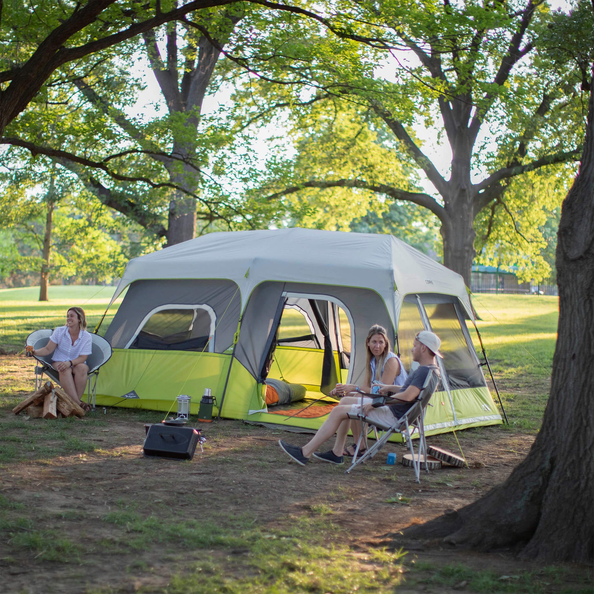 Campers relaxing beside the CORE 9 person instant cabin tent in gray and green, designed for fast setup and reliable weather protection.