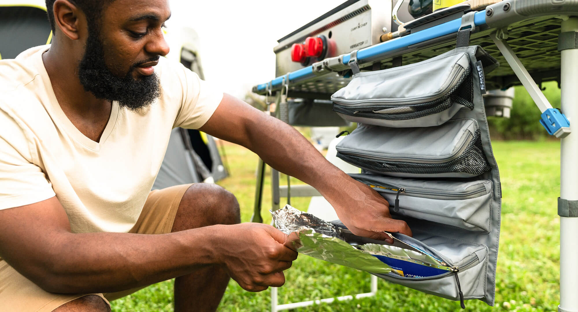 A camper is organizing camping supplies in the FlexRail hanging organizer on the 4 foot FlexRail cook table.