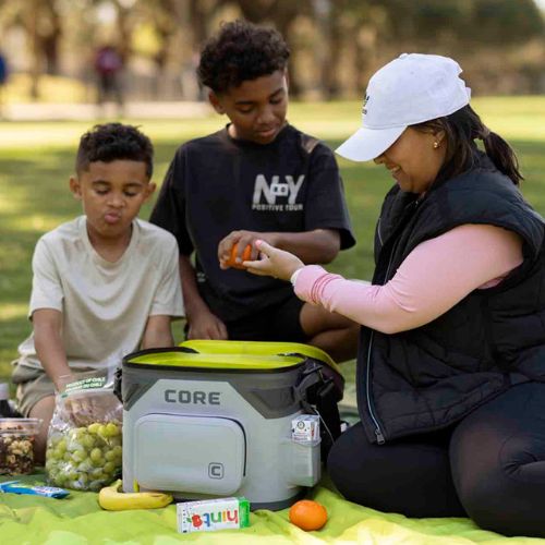 A family sitting on a blanket outdoors with a CORE 18 can soft cooler.