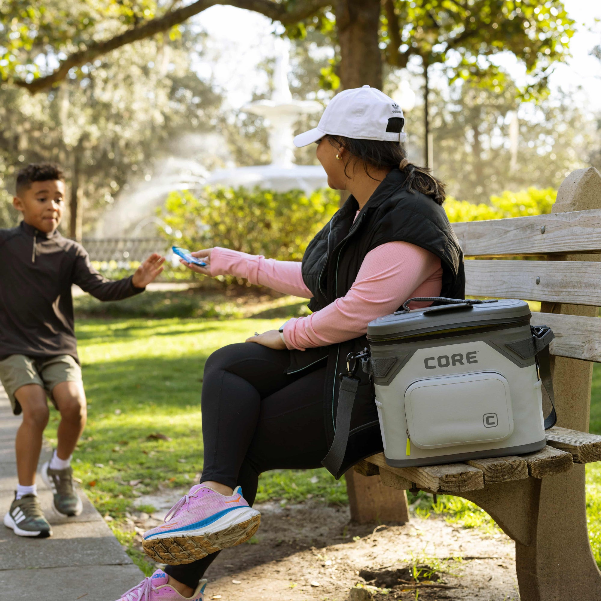 Woman sitting on a park bench with a child, next to a CORE 18 can climakeep soft cooler.