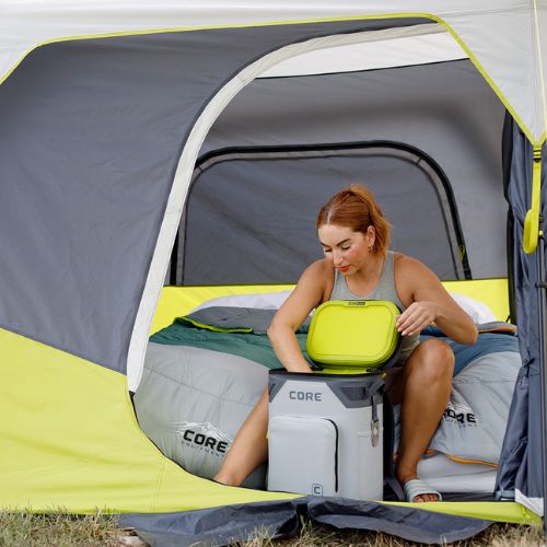 A woman sitting inside a tent with a CORE gray 24 can Climakeep cooler on a camping trip.