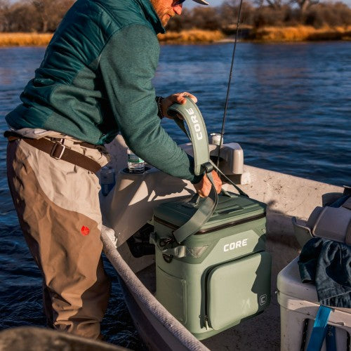 A person on a boat with a green cooler labeled 'CORE' by a body of water.