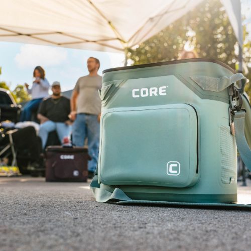 A green soft cooler with 'CORE' branding is sitting on a concrete slab during a tailgate.