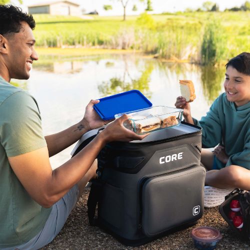 Two people sitting by a lake, eating lunch with a CORE 36 can cooler.