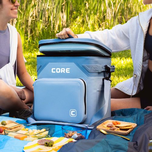 Two people sitting outdoors with a blue CORE cooler, opening it on a CORE weighted blanket.