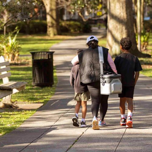 Three people walking on a path in a park carrying a CORE 36 can soft cooler.
