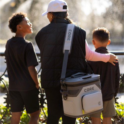 A person with a branded CORE soft cooler bag standing outdoors with two children.