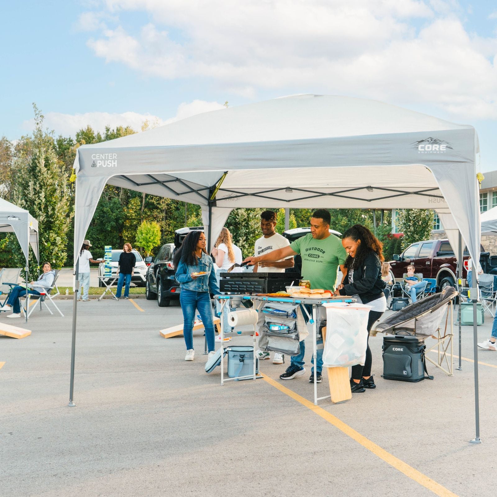 A gray pop-up canopy tent set up in a parking lot, with several people gathered underneath at a market or event. The canopy has visible branding for 'Core' and 'PUSH'.