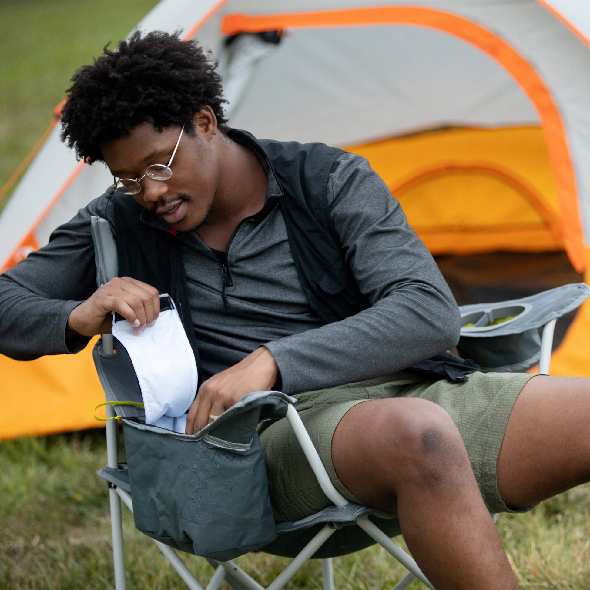 A man sitting in a cooler quad chair, accessing the built-in cooler pocket while camping.