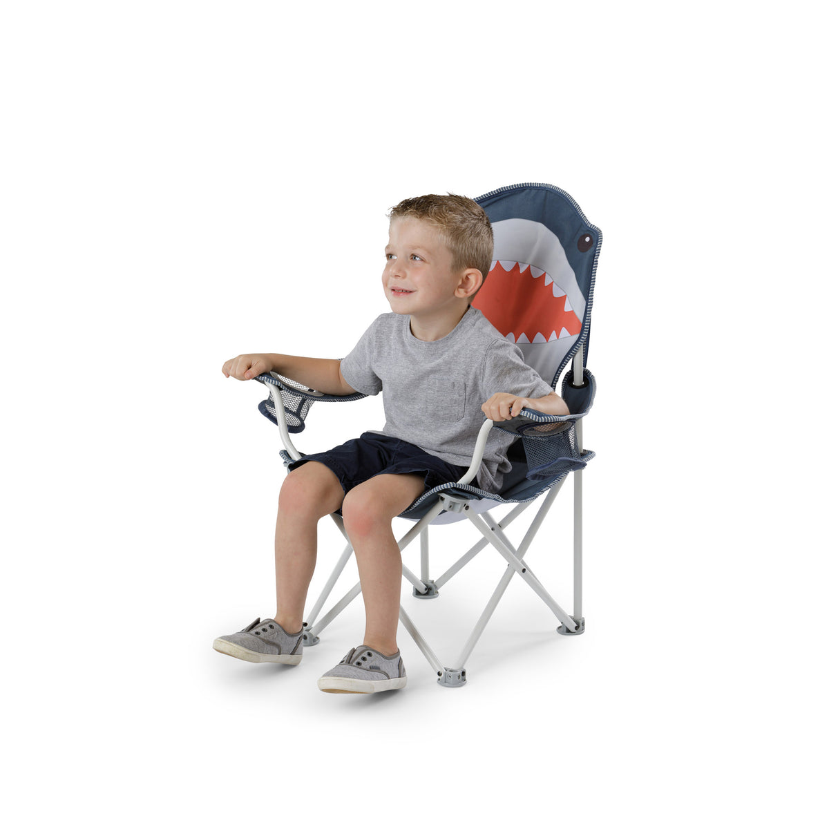 A young boy sitting on a folding camp chair with a shark-themed backrest, featuring a blue, white, and orange design, set against a plain white background.