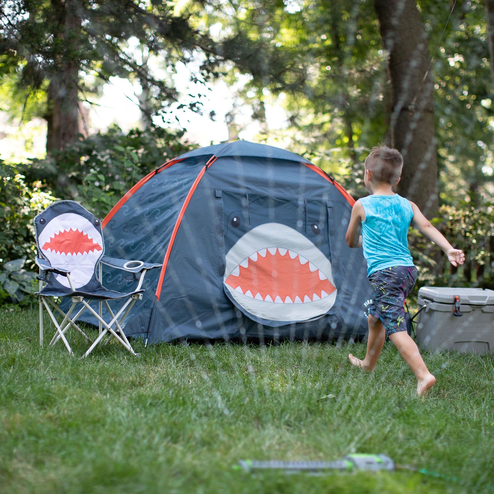 A kid running in the sprinklers next to a FIREFLY! Shark Tent.