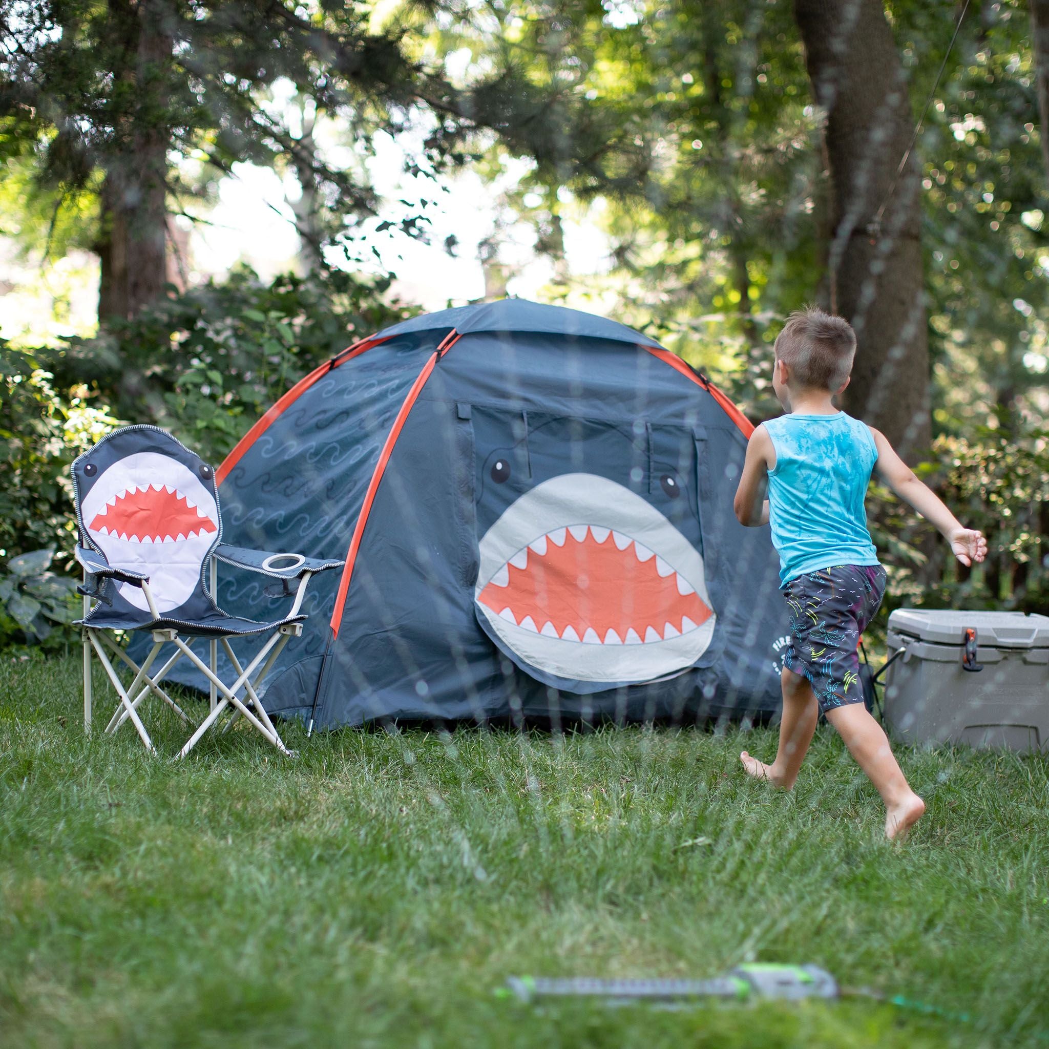 A kid running in the sprinklers next to a FIREFLY! Shark Tent.