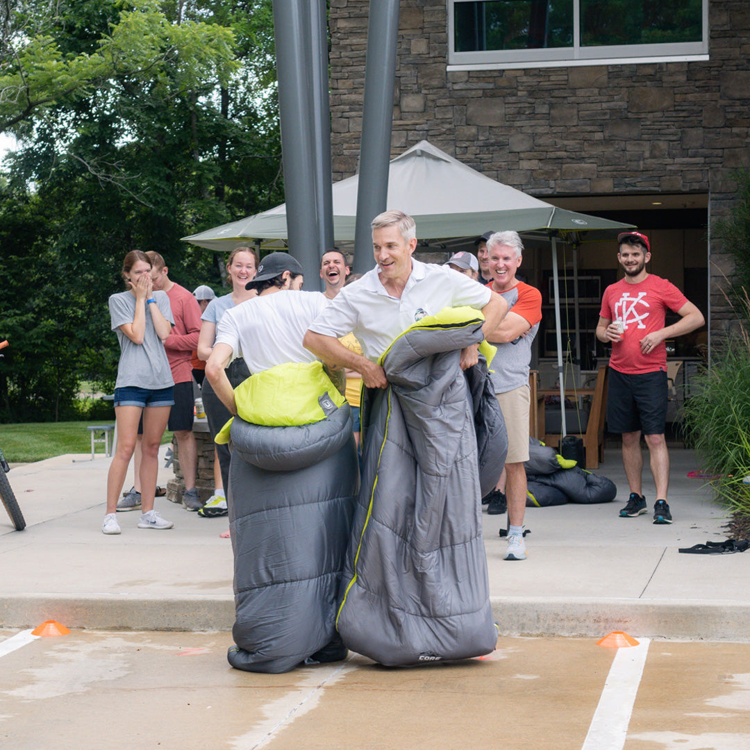 Group enjoying outdoor games as participants race in CORE sleeping bags, highlighting fun and versatile camping gear.