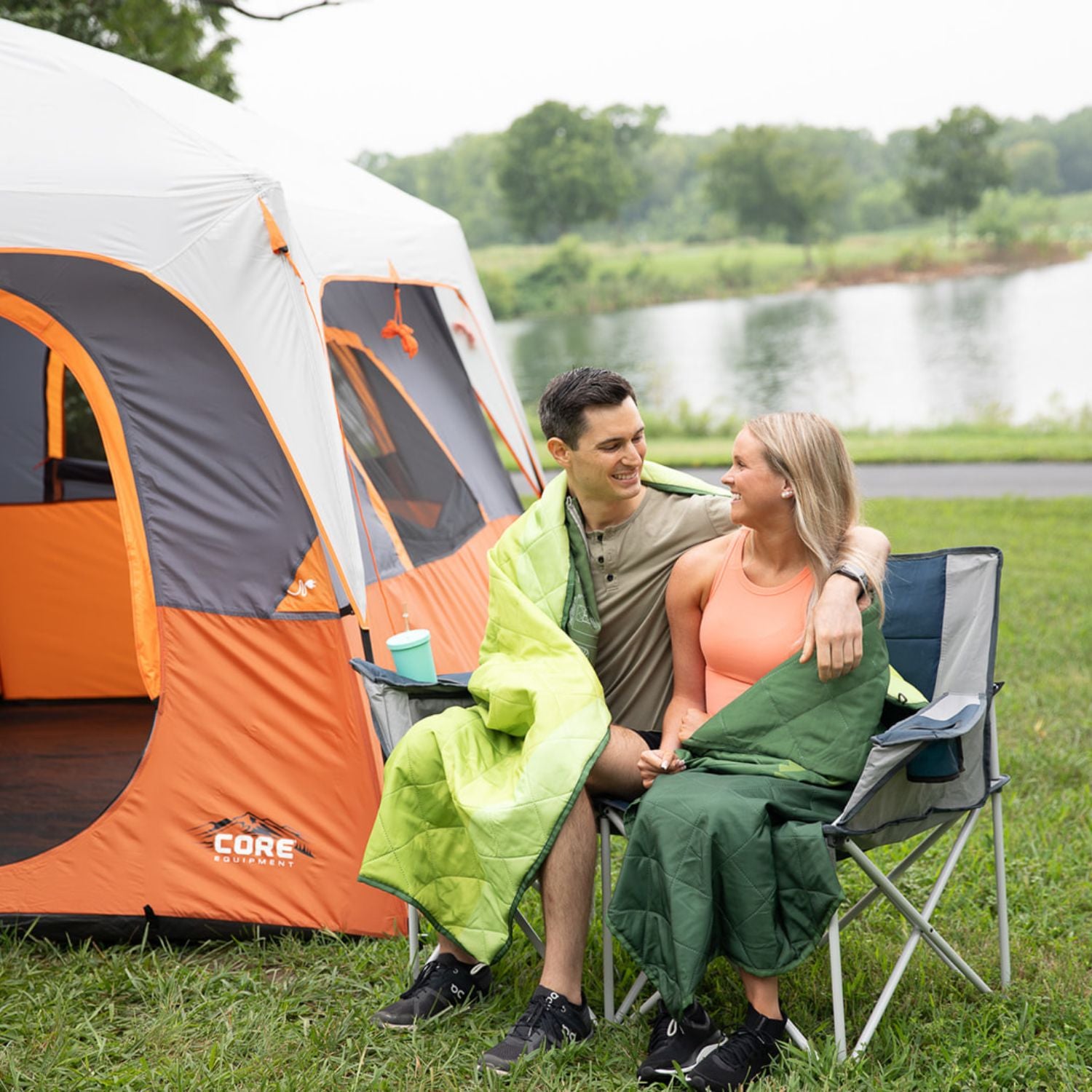 A couple sitting in a CORE loveseat by a CORE 10-person straight-wall cabin tent by a lake.