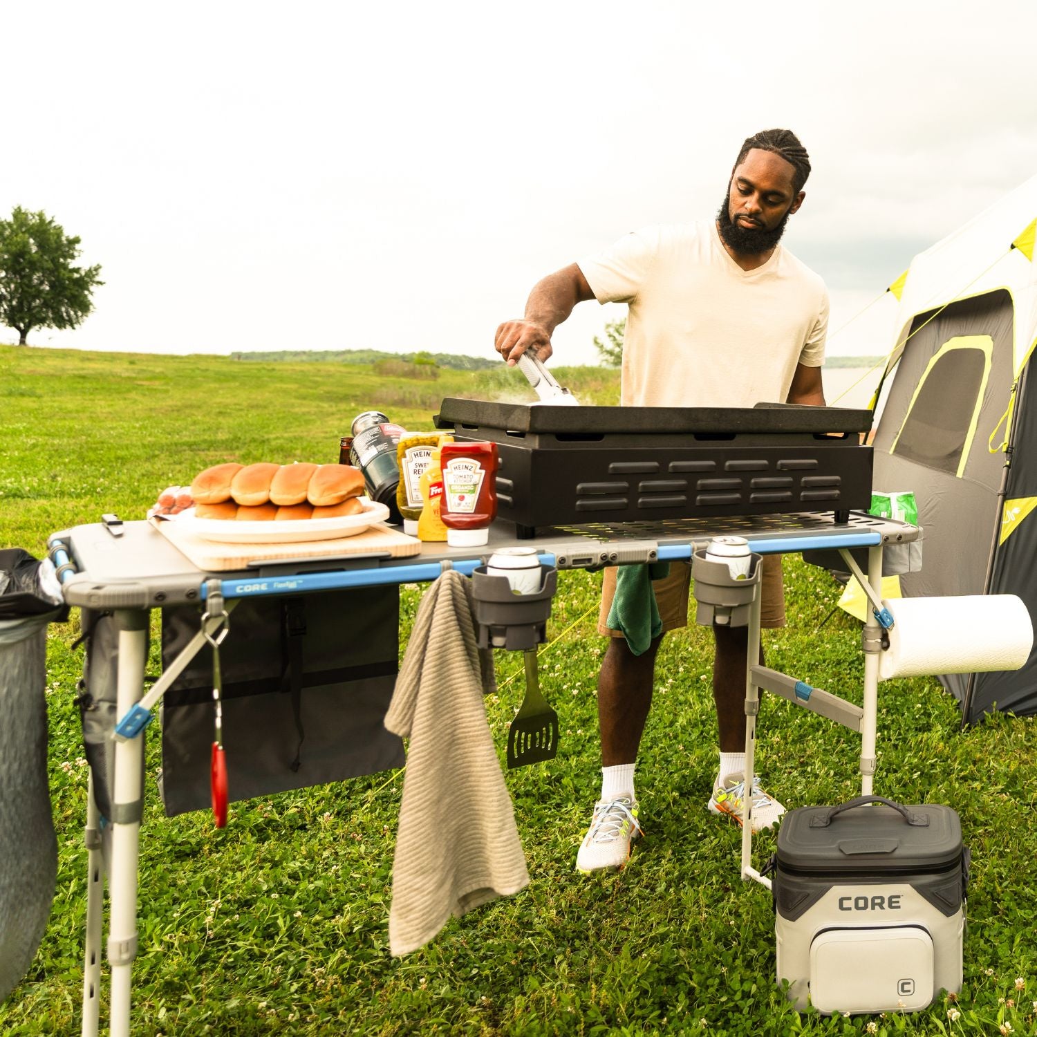 A man grilling outdoors with a CORE 4-foot cook table and a CORE brand cooler.