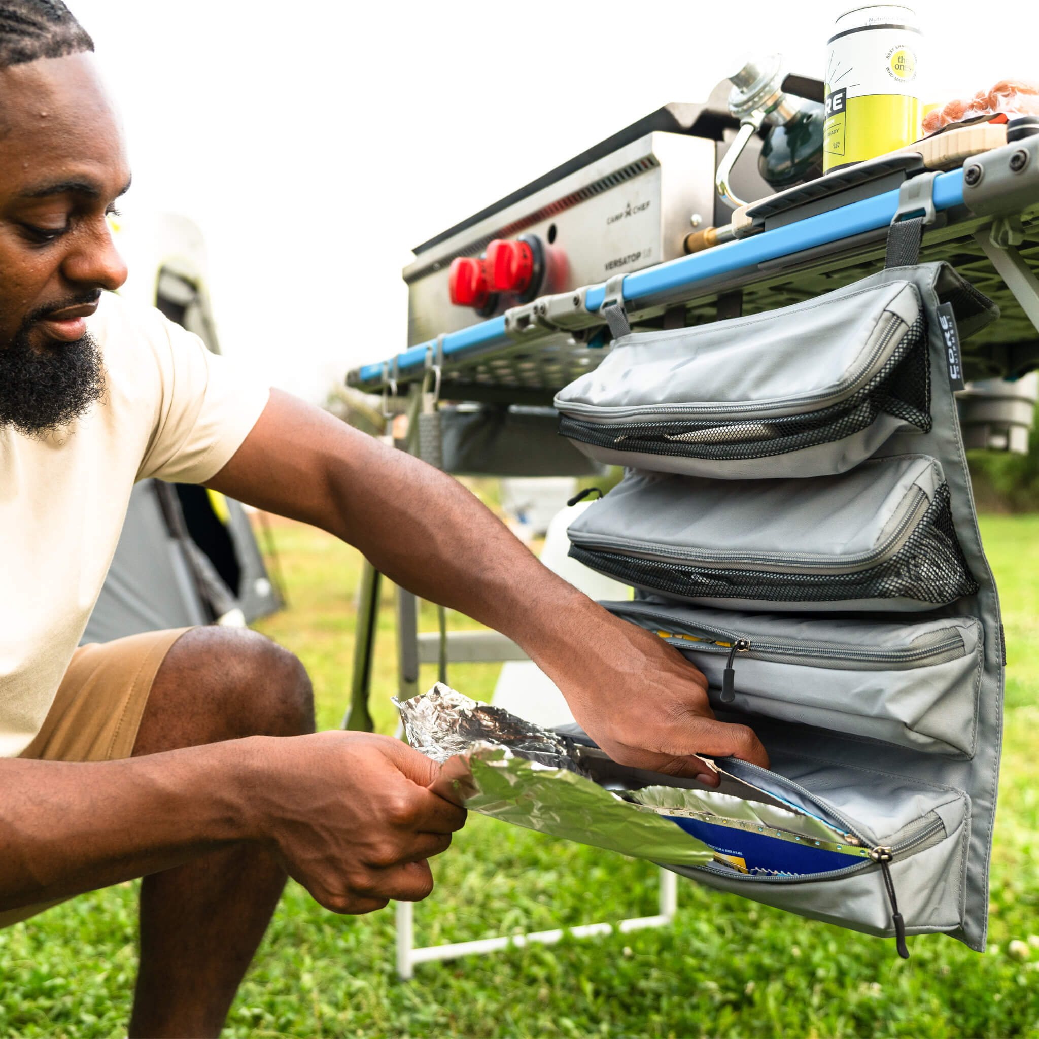 Camper using a CORE hanging organizer on outdoor kitchen table, storing utensils and supplies in zippered compartments.