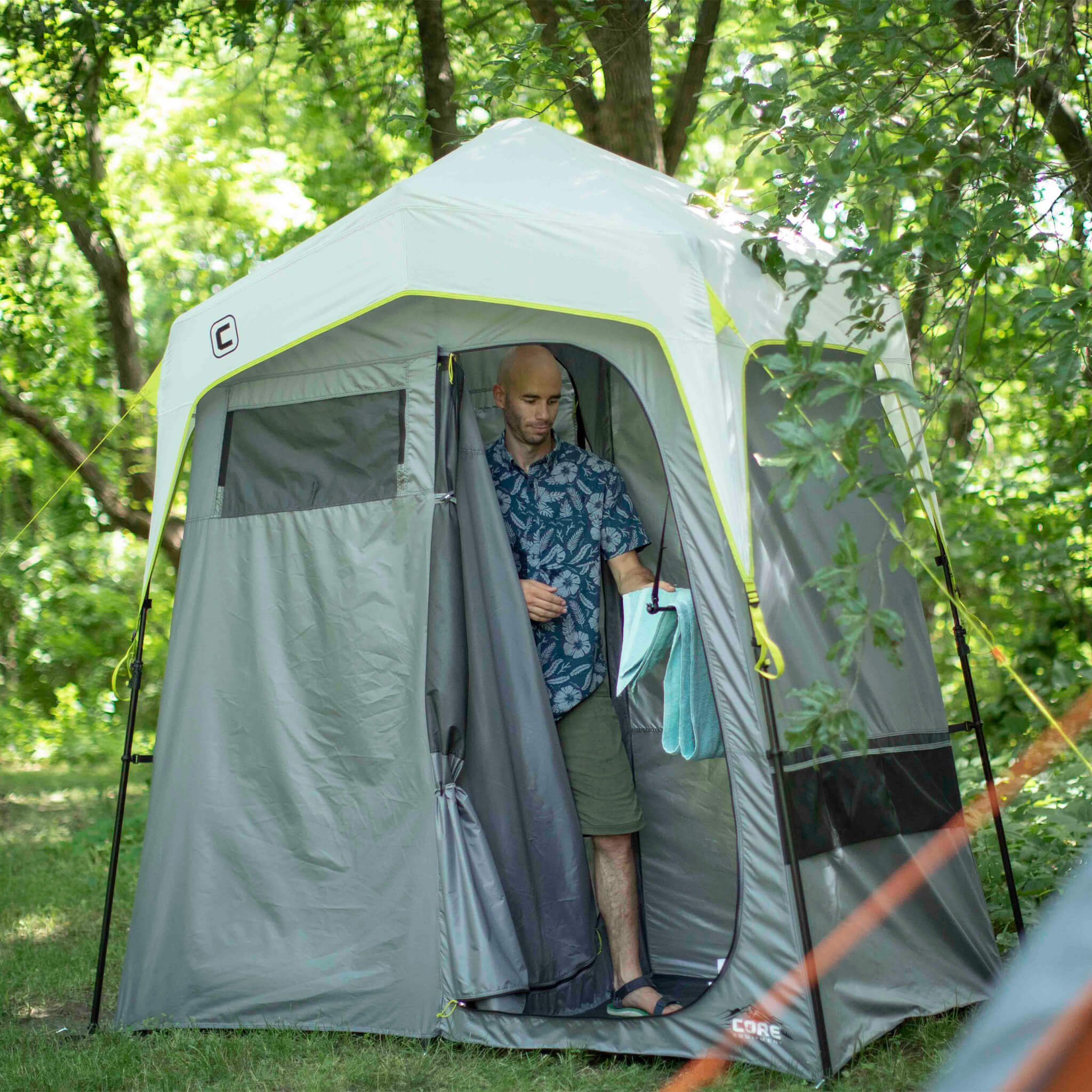 Camper entering the CORE instant shower tent in gray and green, designed for privacy, quick setup, and outdoor convenience.