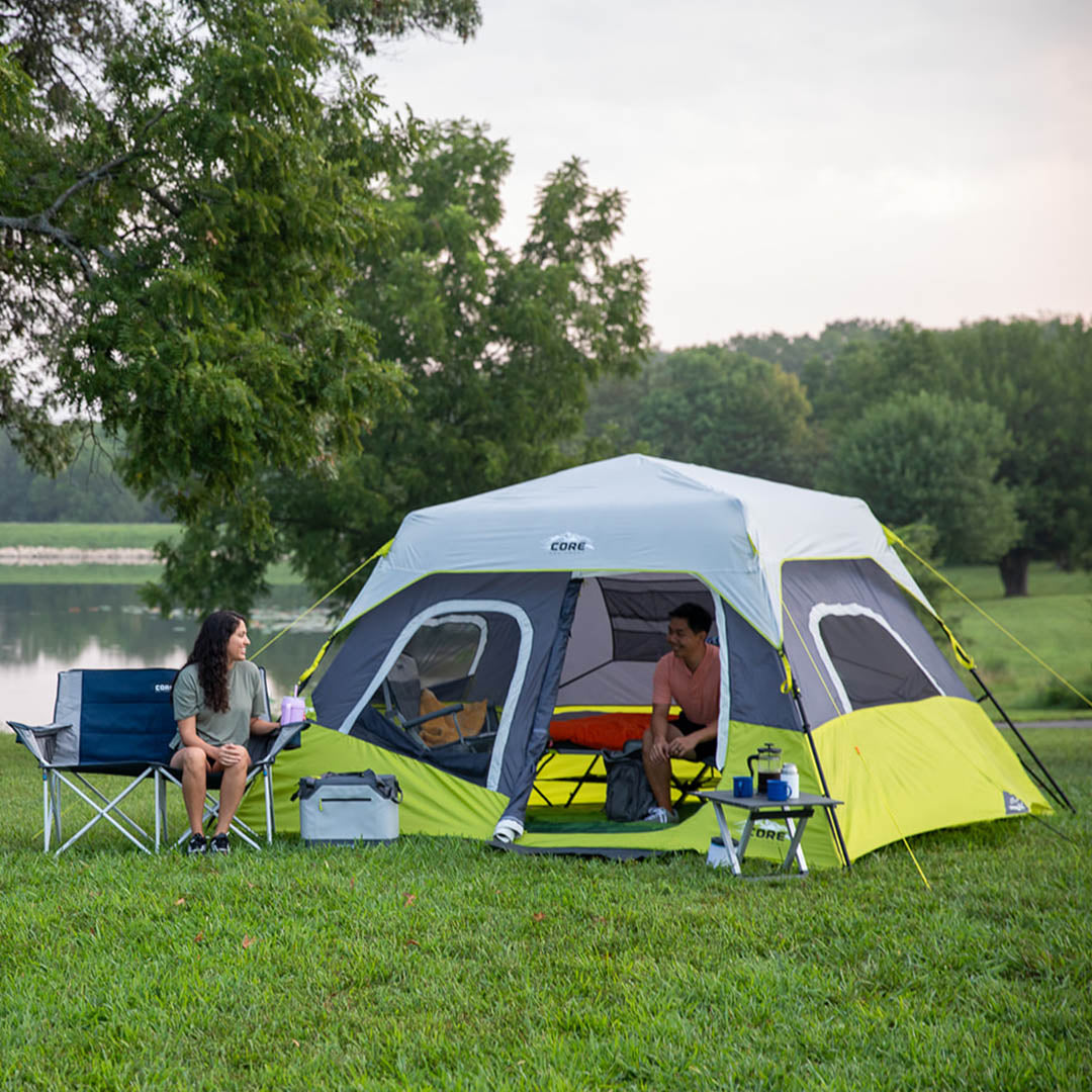 Two people sitting outside a CORE 6 person instant cabin tent by a lake.
