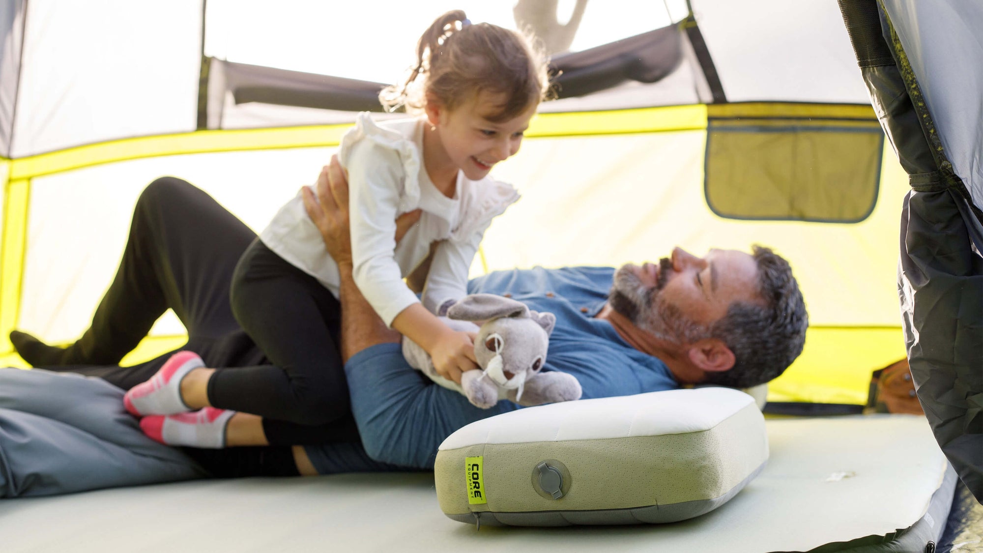 A father and daughter are lying on an inflatable CORE mattress inside a CORE 6 person instant cabin tent.