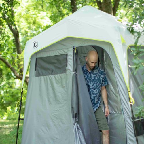 Person standing inside a portable shower tent in a forest setting.