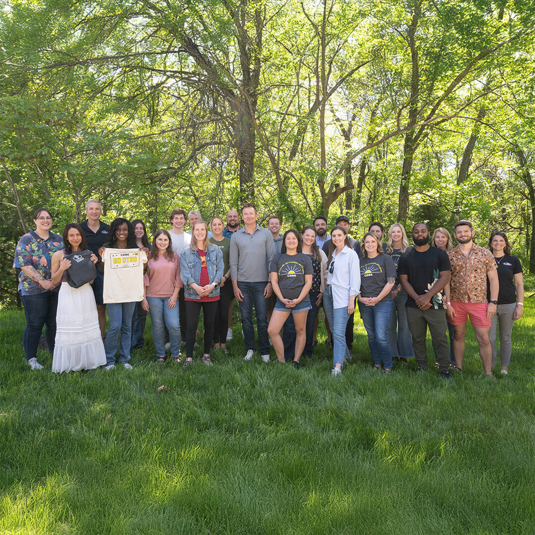 Group of people for CORE Equipment posing for a photo in a park with trees in the background.