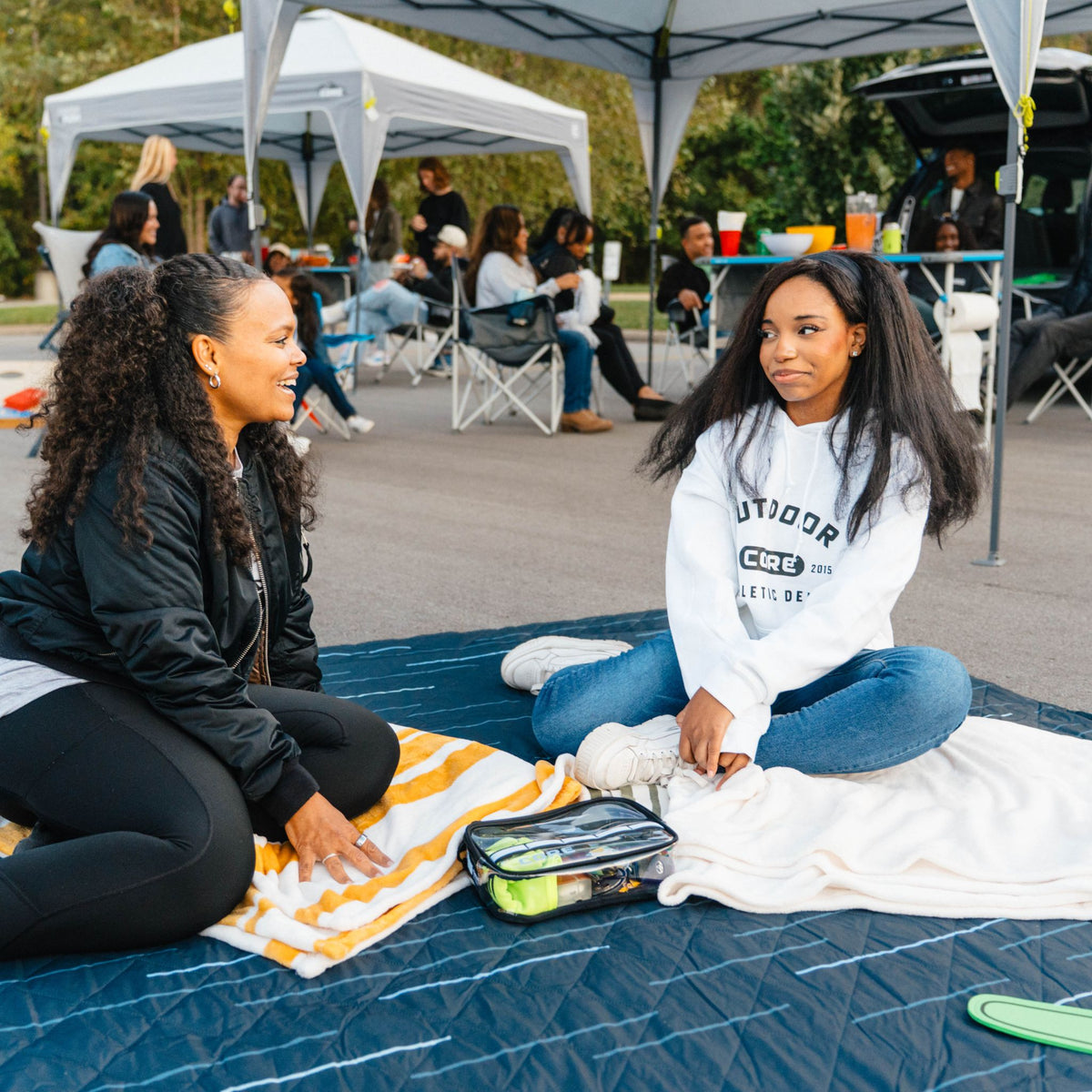 A family sitting on the blanket at a tailgate.