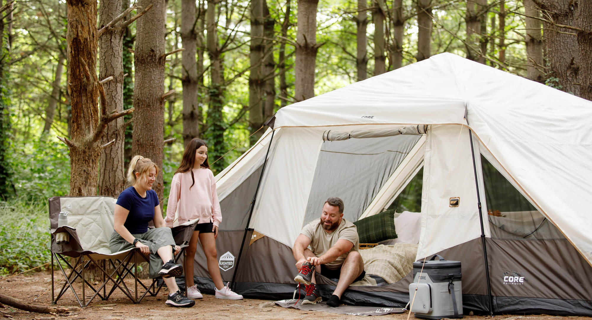 Family relaxing outside a CORE 10 person lighted pyramid tent in the woods.